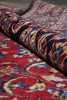 Load image into Gallery viewer, A close-up of a folded patterned rug showing a rich red base with intricate floral and paisley motifs in blue, cream, beige, and brown.