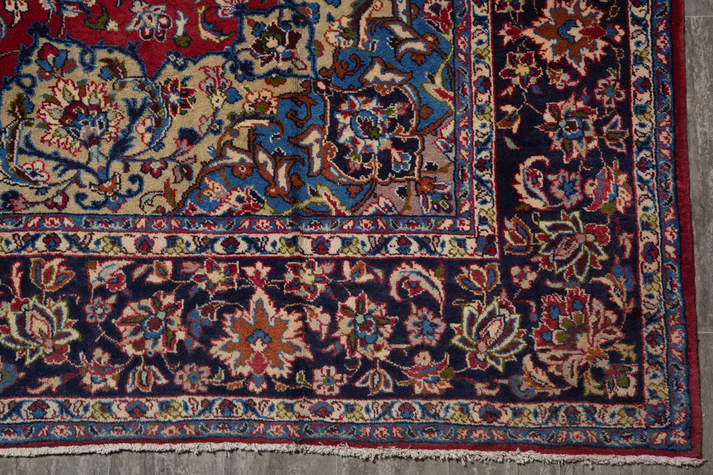 A close-up of a traditional oriental rug corner showing a dark navy blue field with intricate floral and vine motifs in red, beige, blue, and green, finished with a fringed edge.