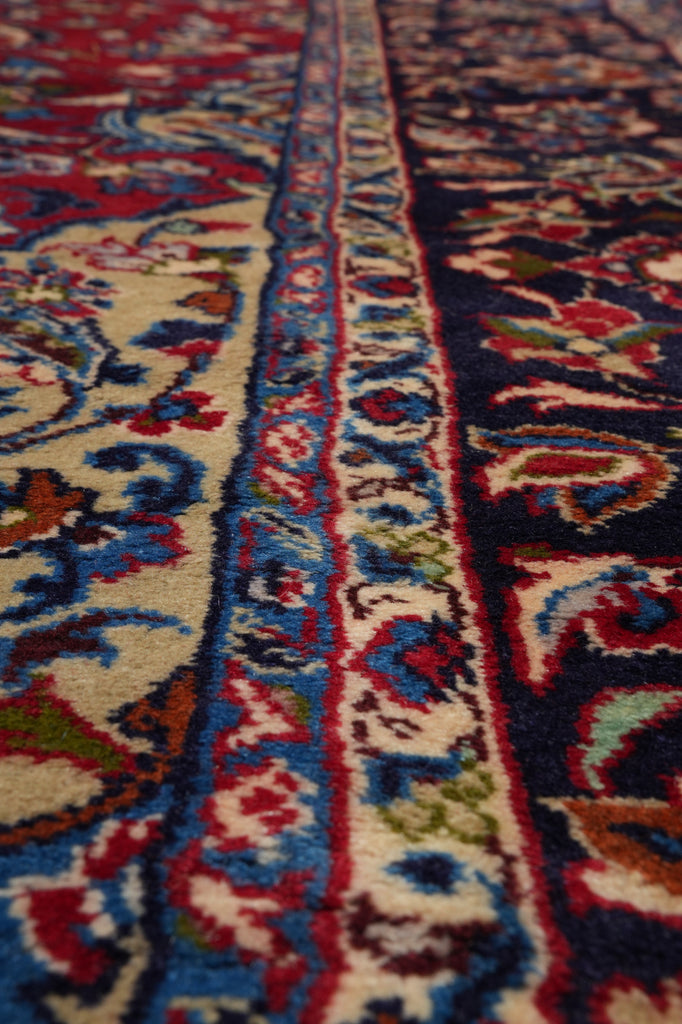 A close-up view of a traditional patterned rug with ornate floral and scroll motifs in cream, red, blue, green, and dark navy tones.