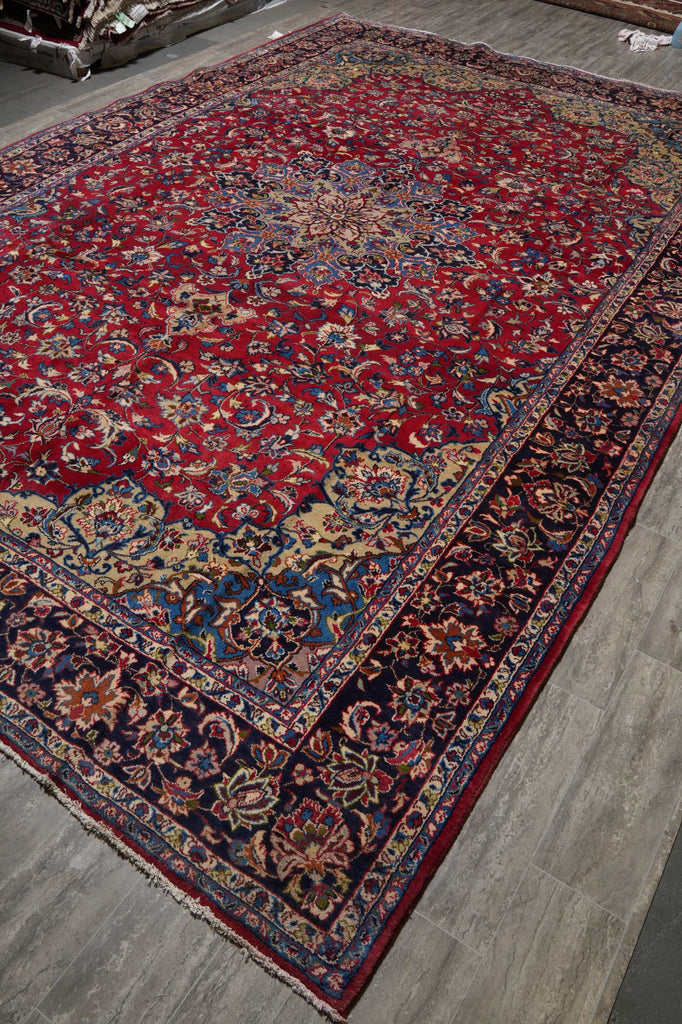 A traditional oriental area rug with a red field, dark navy borders, and intricate floral motifs in blue, gold, and beige.