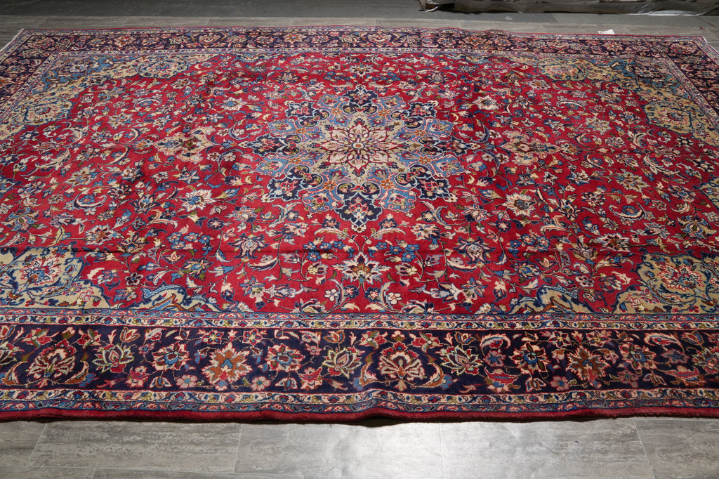 A large traditional oriental area rug with a dominant red field, featuring an intricate floral pattern and a dark navy blue border.