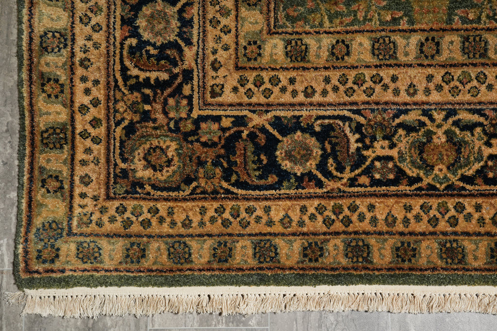 Close-up of an ornate patterned rug corner showing a dark navy and beige floral border with cream fringe along the bottom edge.
