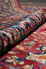 Load image into Gallery viewer, A close-up of a folded patterned rug showing a detailed floral and ornamental design in red, blue, cream, and beige tones.