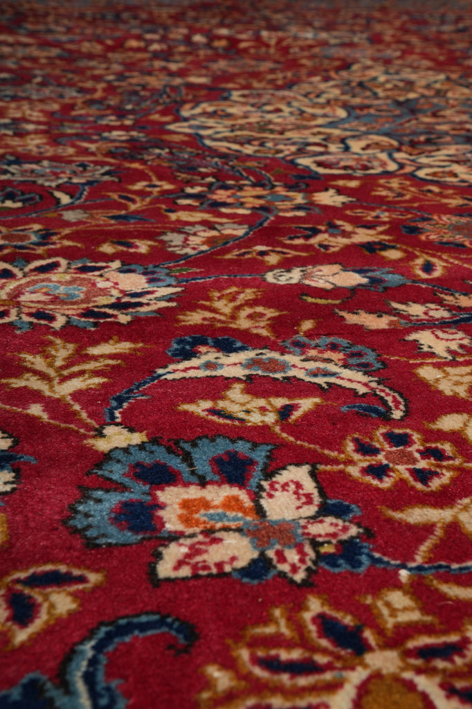 A close-up of a traditional patterned rug with a deep red background and floral motifs in blue, beige, and orange.