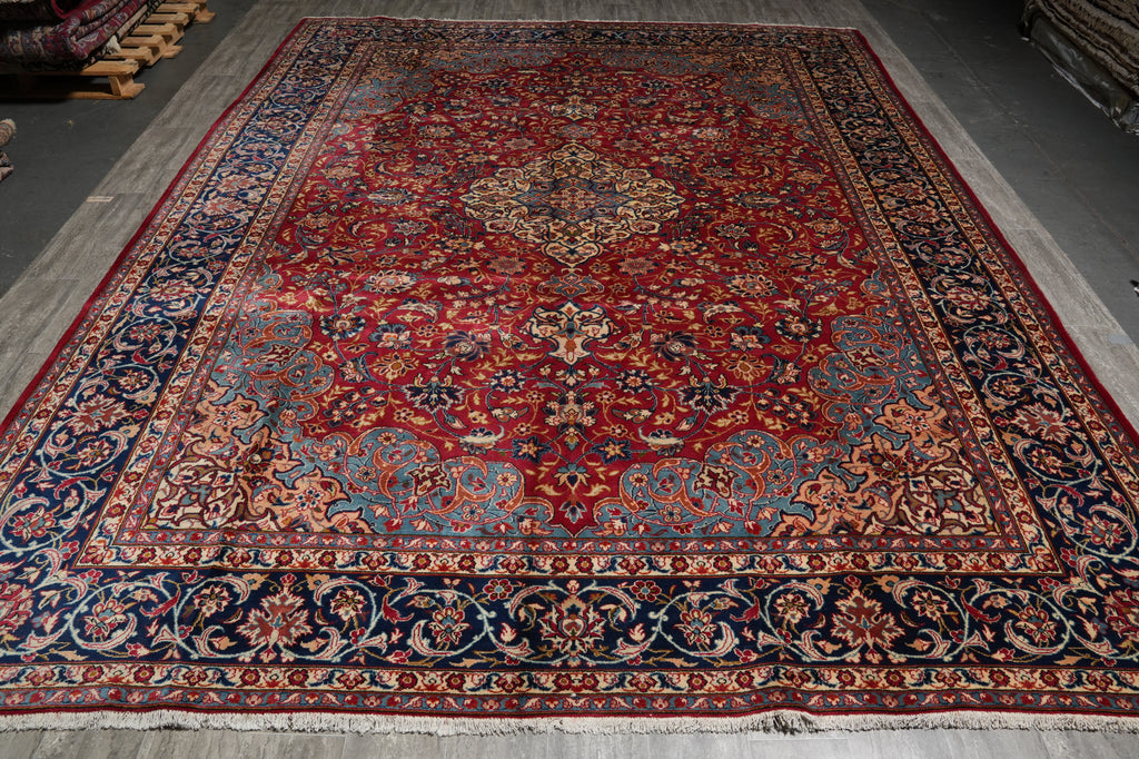 A traditional Persian-style area rug with a complex floral pattern, featuring a dominant red field, a central medallion, and a dark navy blue border with cream accents.