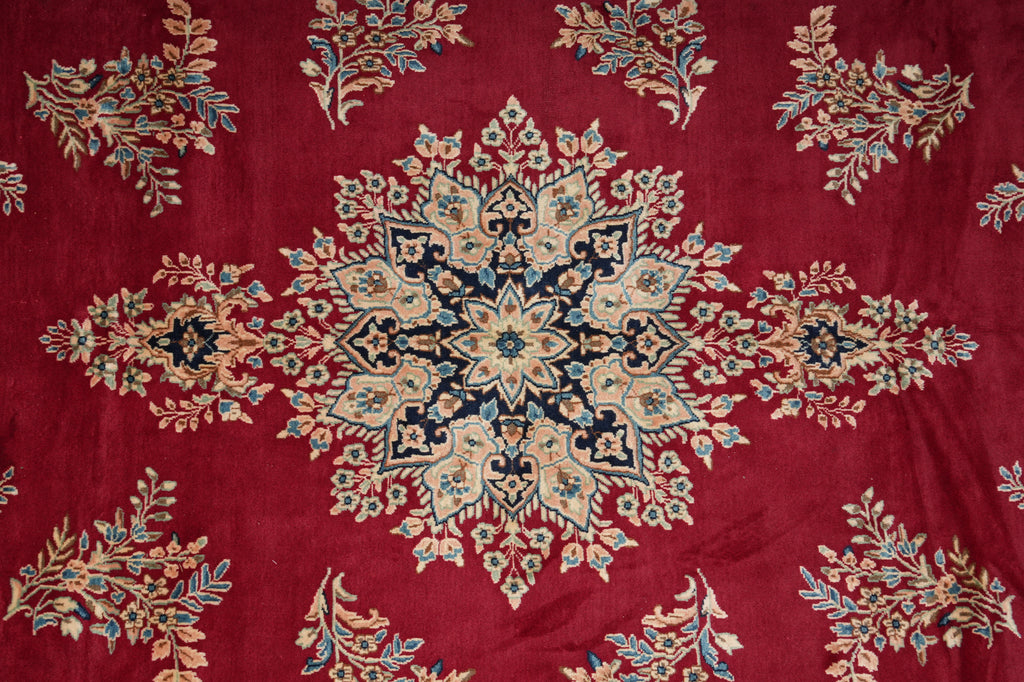A close-up of a red patterned textile or rug featuring a large central medallion and repeating floral motifs in beige, blue, and gold tones.