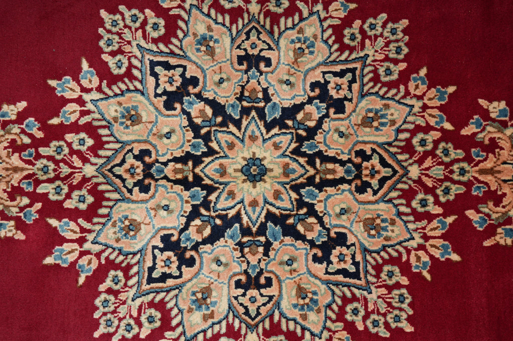 A close-up of a traditional oriental rug featuring a deep red background with a large central medallion in beige, navy blue, and light blue.