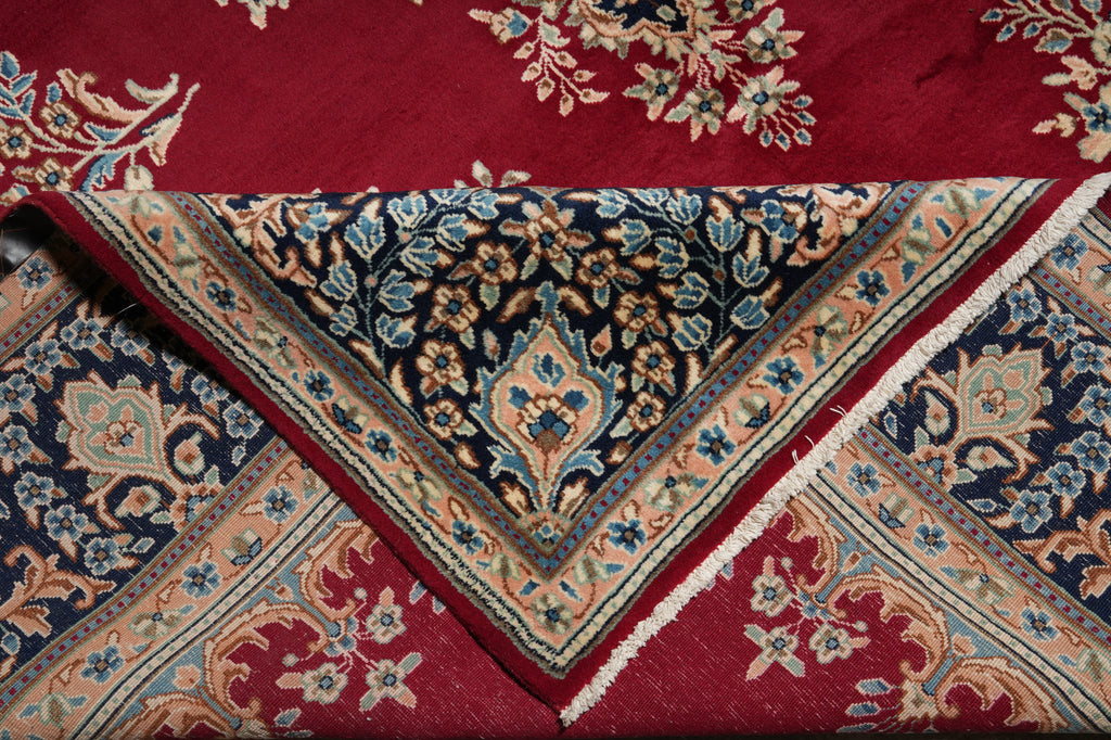A folded traditional patterned rug shown in close-up, featuring a deep red field with floral motifs and a central dark navy section with ornate floral and vine borders in beige, blue, and red.