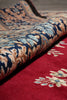 Load image into Gallery viewer, Close-up of a patterned rug with a rolled section showing a red field, cream floral motifs, and a central pattern in navy blue, tan, and light blue.