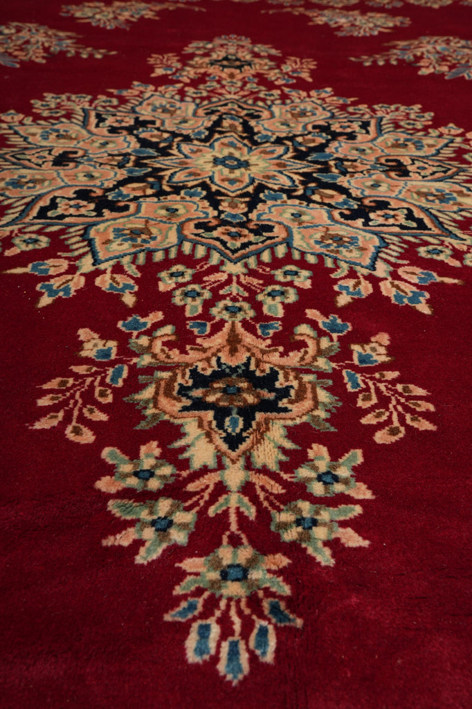 A close-up of a traditional oriental rug featuring a deep red background with an intricate floral and medallion pattern in beige, blue, and black.