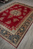 Load image into Gallery viewer, A traditional oriental area rug with a deep red field, beige and navy blue floral motifs, and ornate borders, shown laid out on a gray wood-look floor.