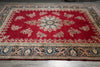 Load image into Gallery viewer, A traditional oriental area rug with a vibrant red field, featuring a central floral medallion and ornate borders in navy blue, beige, and gold, laid out on a gray tiled floor.