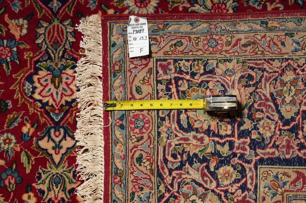 A close-up of an ornate patterned rug with cream fringe, shown with a yellow tape measure and a white size tag to indicate dimensions.