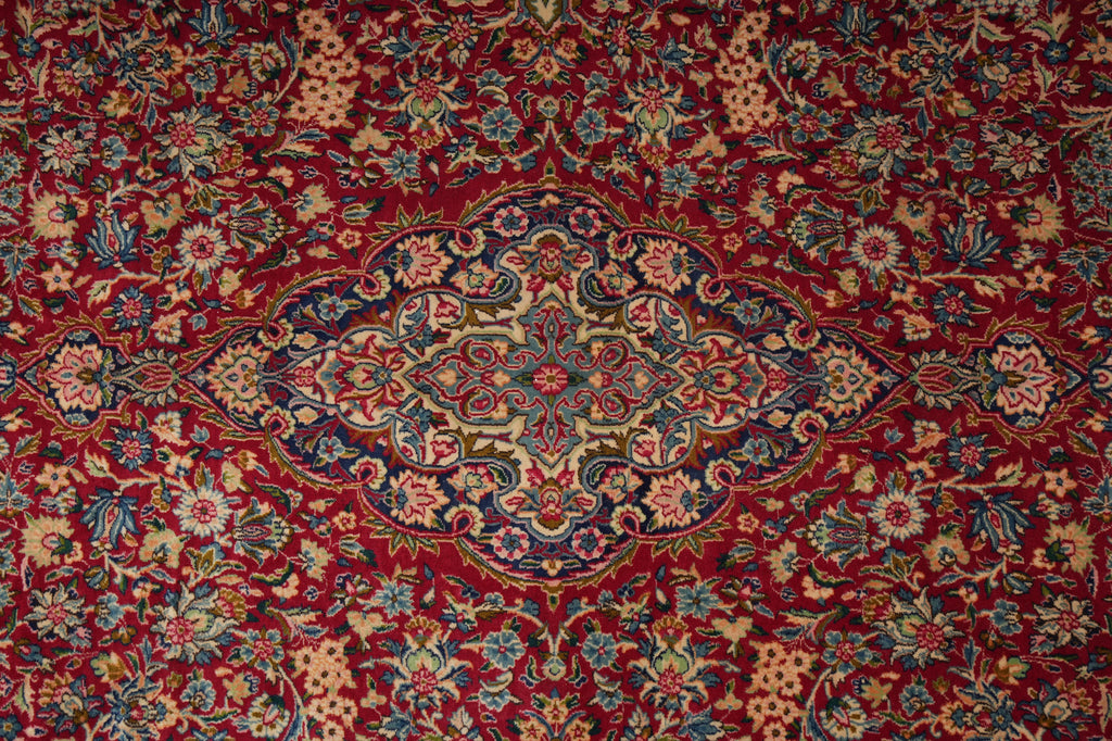 A close-up of a traditional Persian-style area rug featuring a rich red background with an intricate central medallion and floral motifs in beige, blue, and green.