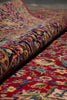 Load image into Gallery viewer, A close-up of a rolled area rug showing its intricate traditional pattern in red, beige, blue, green, and yellow tones.