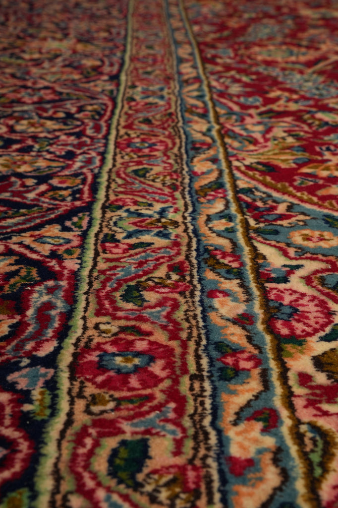 Close-up of an ornate patterned rug with red, blue, beige, and green floral motifs and detailed woven borders.
