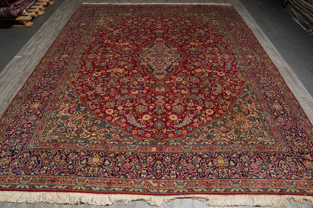 A traditional Persian-style area rug with a deep red central field, intricate floral motifs, and detailed borders, shown laid out on a gray floor.