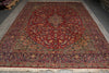 Load image into Gallery viewer, A traditional Persian-style area rug with a deep red central field, intricate floral motifs, and detailed borders, shown laid out on a gray floor.