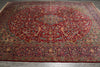 Load image into Gallery viewer, A large traditional Persian-style area rug with a dominant deep red field, featuring an intricate central medallion and detailed floral motifs in blue, green, beige, and gold, laid out on a gray tiled floor.