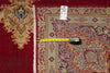 Load image into Gallery viewer, A close-up of a patterned area rug with a deep red field, beige and blue ornamental motifs, and white fringe, shown with a yellow tape measure and a small inventory tag.