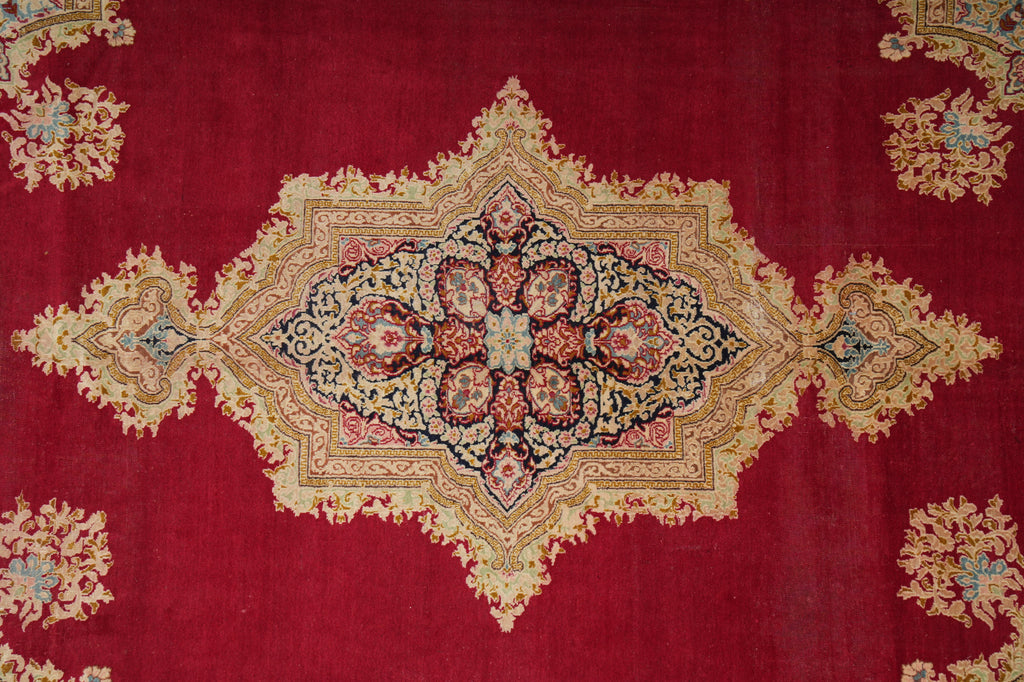 A close-up of a traditional oriental rug featuring a deep red field with a large central diamond medallion and corner motifs in beige, gold, blue, and pink.