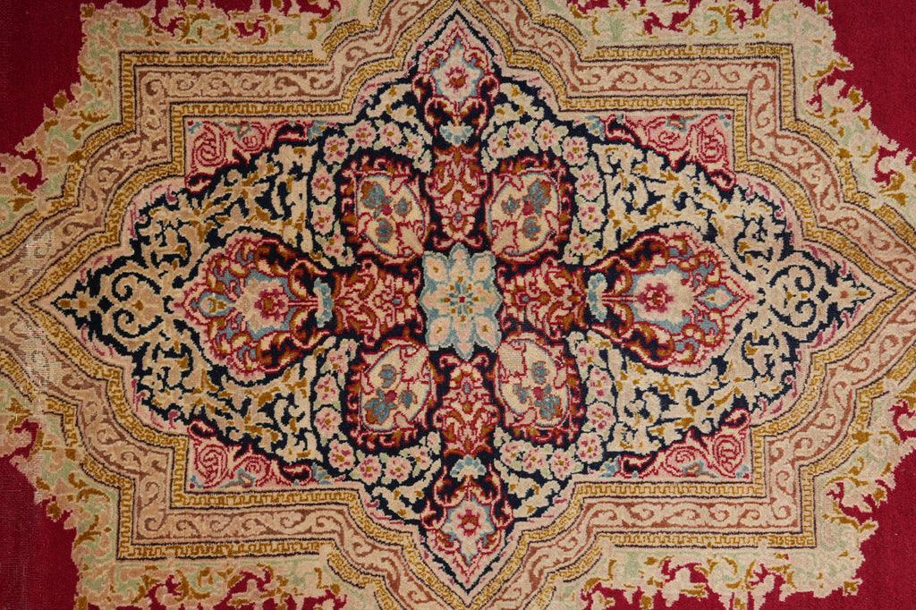 An ornate traditional oriental rug with a large central medallion, featuring a complex floral and scroll pattern in red, beige, navy blue, and gold.