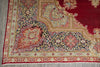 Load image into Gallery viewer, A close-up of an ornate traditional area rug showing its corner detail, featuring a deep red field, a navy blue central field, and cream, gold, and pink floral patterns.