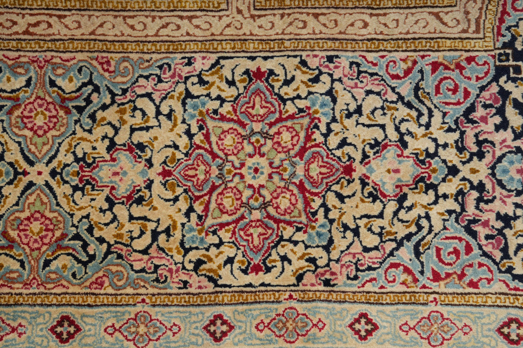 A close-up of an ornate traditional rug with a central floral medallion and intricate scrolling patterns in beige, navy, red, light blue, and gold.