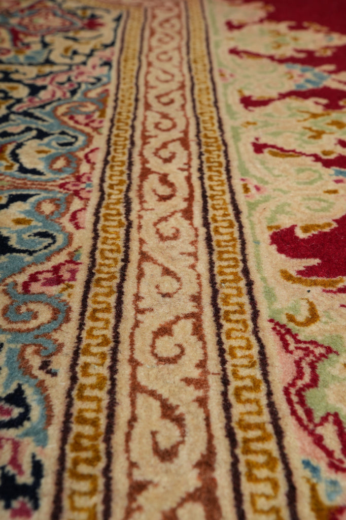 Close-up of an ornate patterned rug showing detailed woven bands in cream, burgundy, gold, blue, and red.