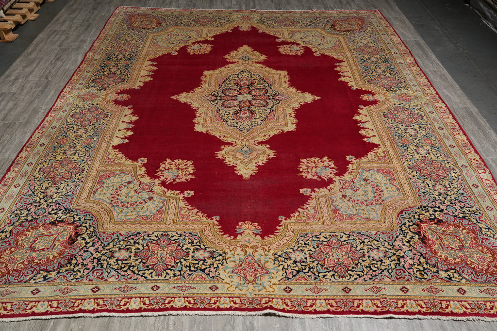 A traditional oriental area rug with a deep red central field, ornate floral motifs, and a detailed multi-colored border, laid out on a gray floor.