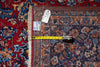 Load image into Gallery viewer, A close-up of a patterned area rug corner with fringe, showing a yellow tape measure and product tag against a red and blue patterned rug.