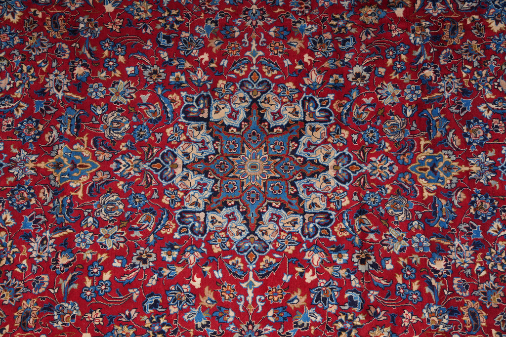 A close-up of a traditional Persian-style rug with a vibrant red background, featuring an intricate central medallion and dense floral motifs in blue, beige, and white.