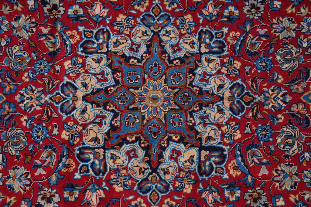 A close-up of a traditional Persian-style rug featuring a vibrant red field with an intricate central medallion and floral motifs in blue, beige, and brown.