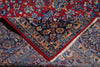 Load image into Gallery viewer, A folded traditional oriental rug with a red field, dark navy central panel, and detailed floral motifs in blue, beige, and gold, showing white fringe on one corner.