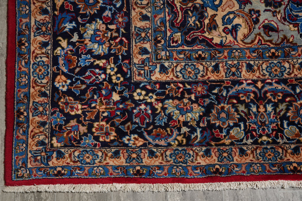 A close-up of a traditional Persian-style area rug showing its detailed floral pattern, deep navy blue field, and red and beige borders with white fringe.