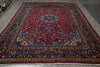 Load image into Gallery viewer, A traditional Persian-style area rug with a deep red central field, detailed blue and beige floral motifs, and an ornate multi-colored border, shown laid out on a gray floor.