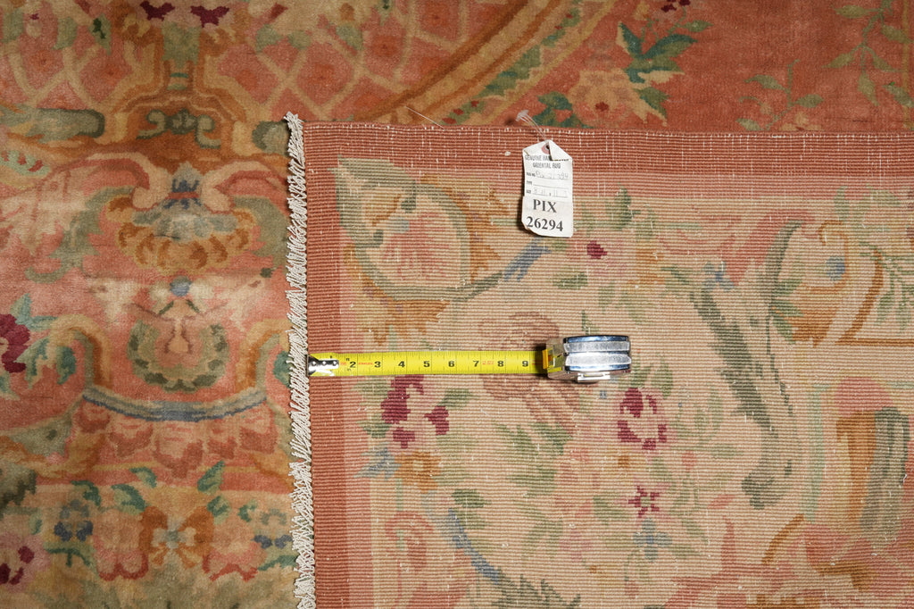 A close-up of a patterned area rug with a measuring tape laid across the corner and a small inventory tag attached, showing the rug's detail and scale.