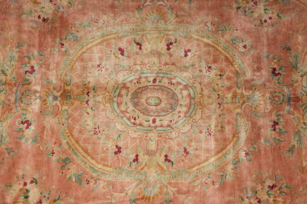 A square area rug with a faded medallion pattern in dusty pink, beige, and muted teal-green.