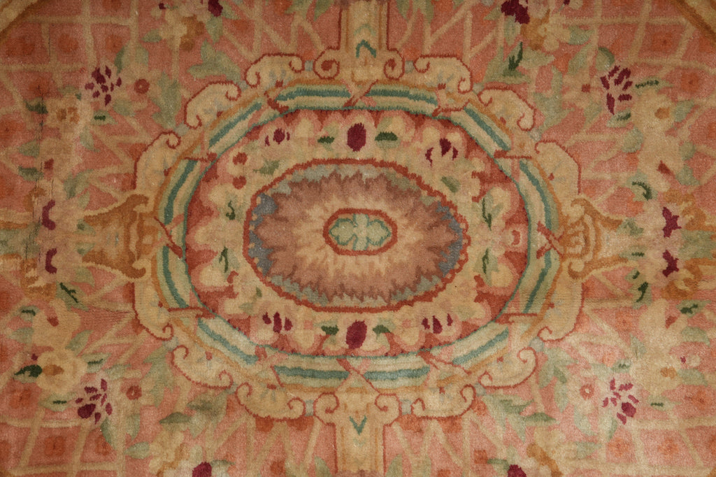 A close-up of a traditional oriental rug featuring a central oval medallion and surrounding floral motifs in muted pink, beige, sage green, and terracotta.