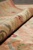 Load image into Gallery viewer, A close-up of a rolled area rug showing its detailed pattern and texture. The rug features a soft, warm beige base with a traditional floral motif in muted shades of pink, sage green, and red.