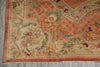 Load image into Gallery viewer, A close-up of an ornate traditional rug corner, showing a peach and beige field with floral motifs, green foliage, and a peach border, laid on a gray floor.