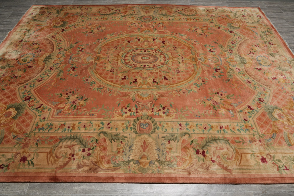 A large rectangular area rug with an ornate medallion pattern in muted terracotta, beige, and sage green tones, laid flat on a gray wood floor.