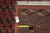 Load image into Gallery viewer, A close-up of a patterned area rug with a red field, dark navy geometric border, and cream fringe, shown alongside another red patterned rug and a yellow tape measure for scale.