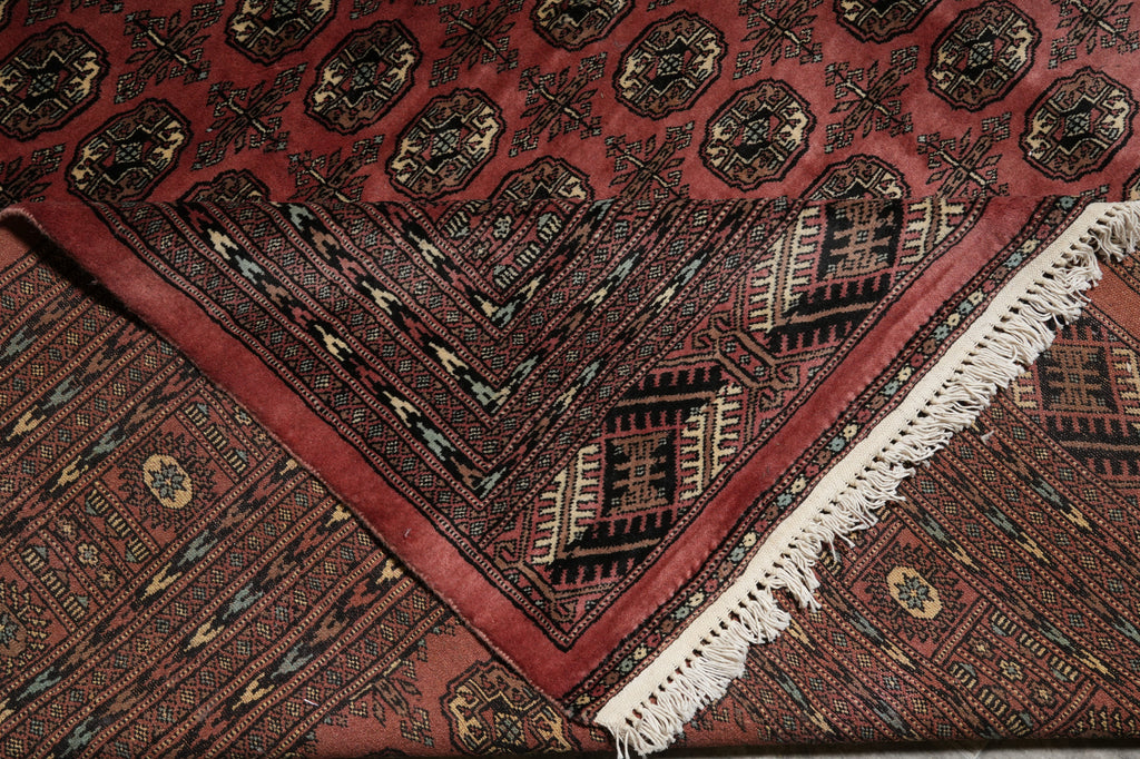 A close-up of a patterned area rug with a deep red field, black and beige geometric motifs, and white fringe along one corner.
