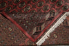 Load image into Gallery viewer, A close-up of a patterned area rug with a deep red field, black and beige geometric motifs, and white fringe along one corner.