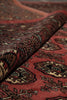 Load image into Gallery viewer, A close-up of a patterned rug or textile with a dusty red background and intricate black, beige, and brown motifs, shown with a folded section revealing the woven texture.