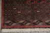 Load image into Gallery viewer, A close-up of a traditional patterned rug corner, showing a deep red field with black, beige, and cream geometric borders and white fringe tassels along the bottom edge.