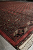 Load image into Gallery viewer, A close-up of a patterned area rug with a deep red field, dark navy borders, and cream fringe, photographed on a gray floor.