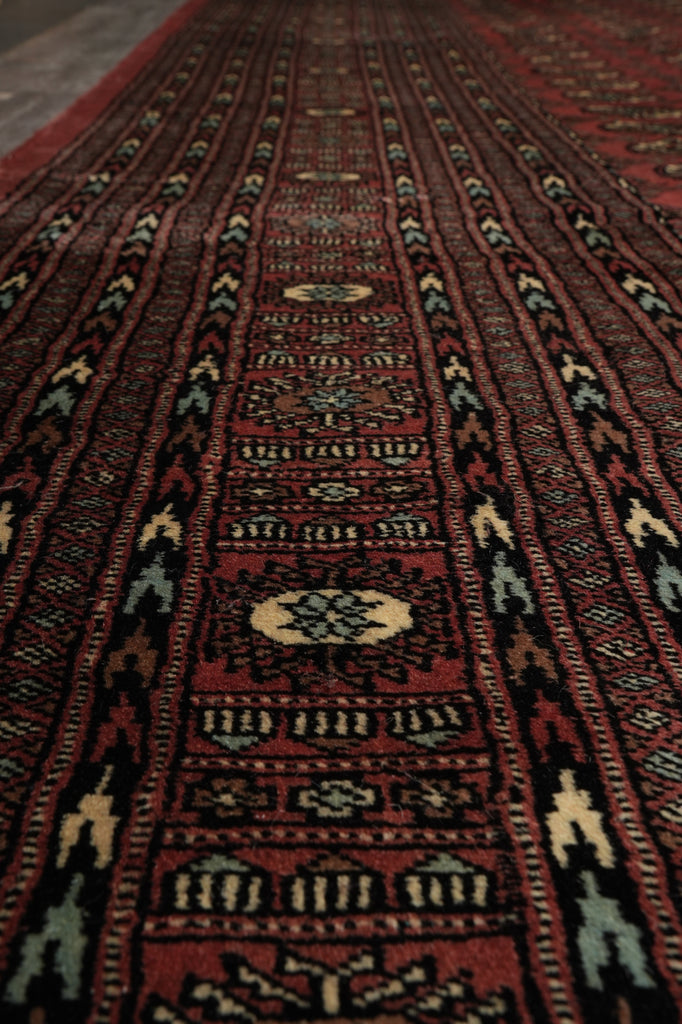 A close-up view of a traditional patterned rug with a deep red field, black borders, and cream and light blue geometric motifs.