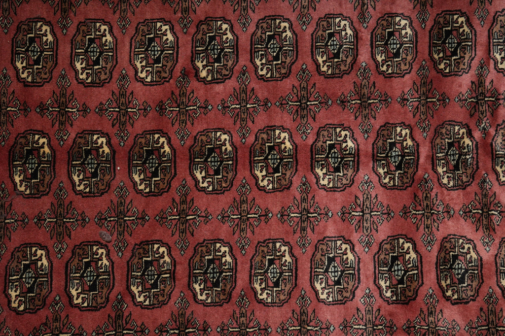A close-up of a patterned textile or rug featuring a repeating medallion design in dark brown, black, and beige on a muted red background.